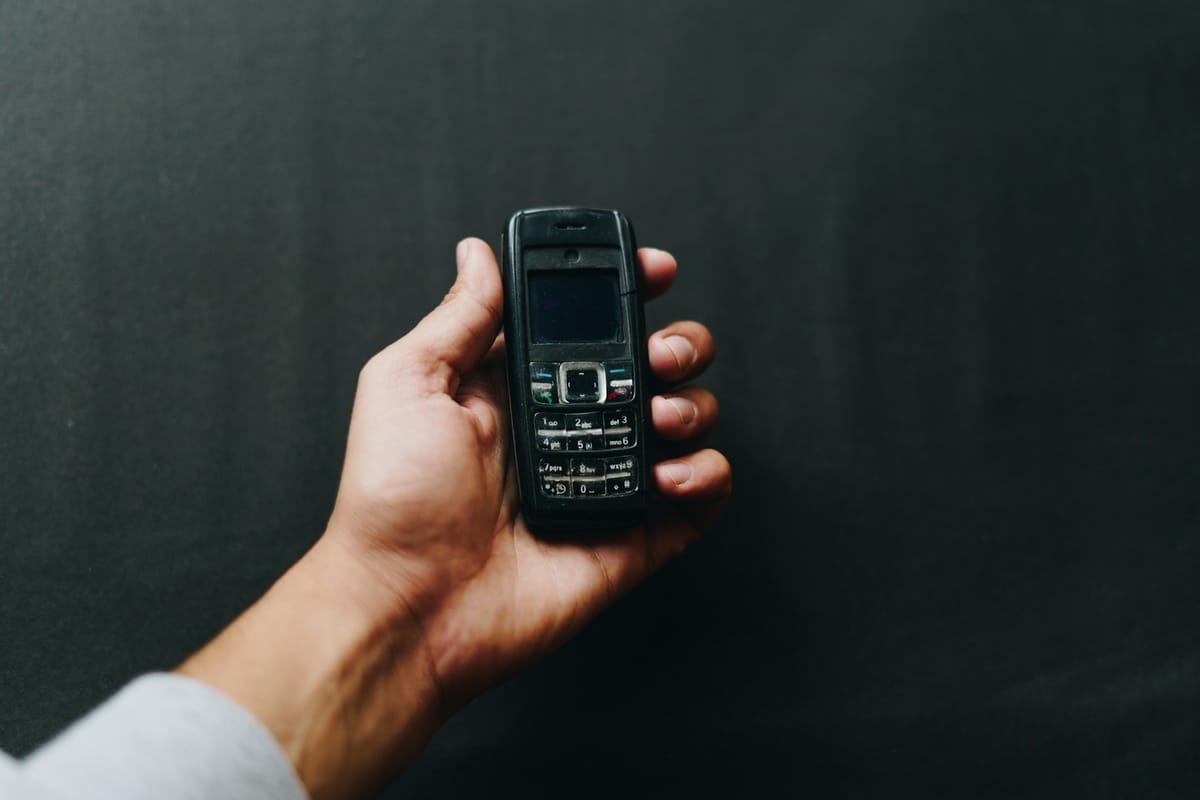 A hand holding a black Nokia keypad phone