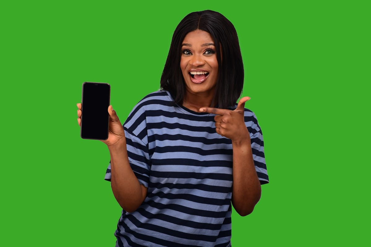 A delighted woman pointing at her phone against a green background