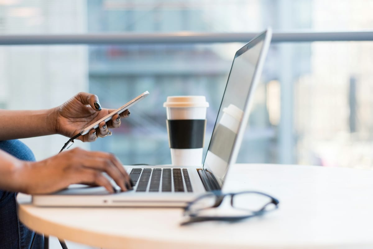 A person using a phone and a laptop at a table