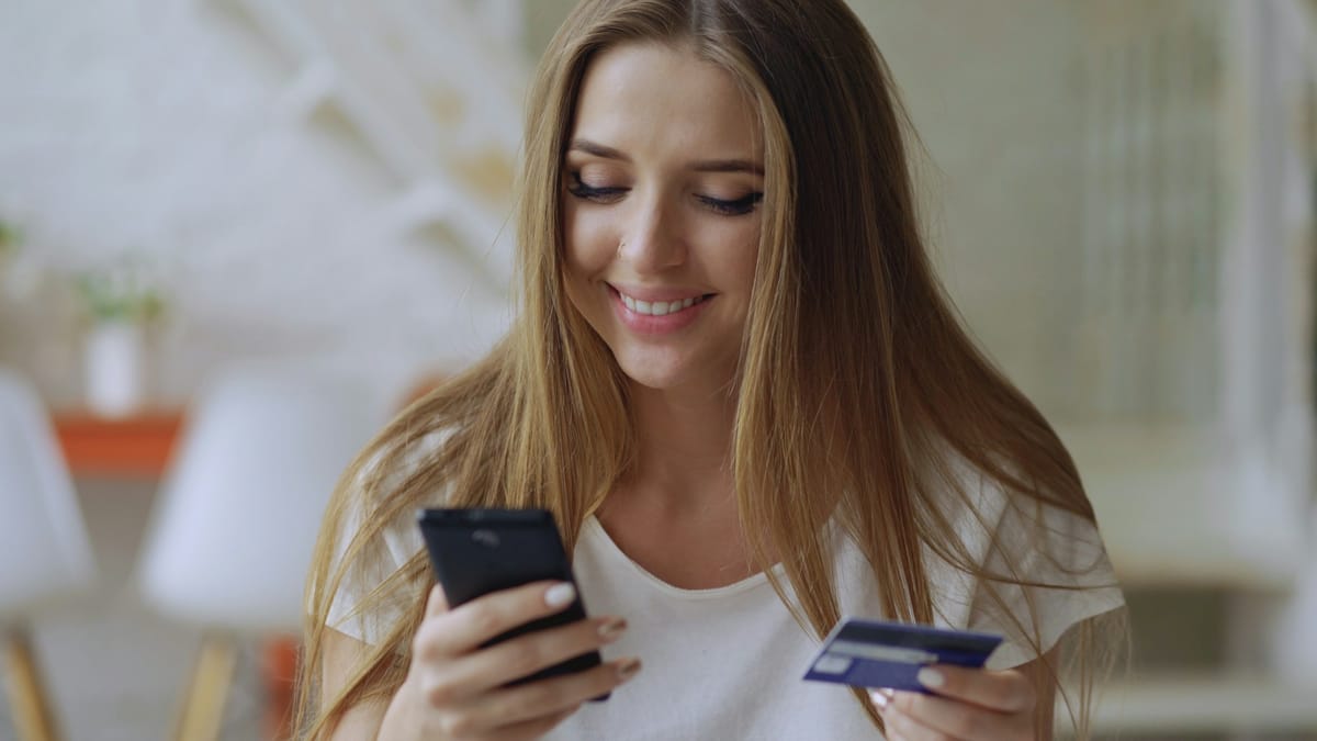 A young woman holding a phone and a bank card