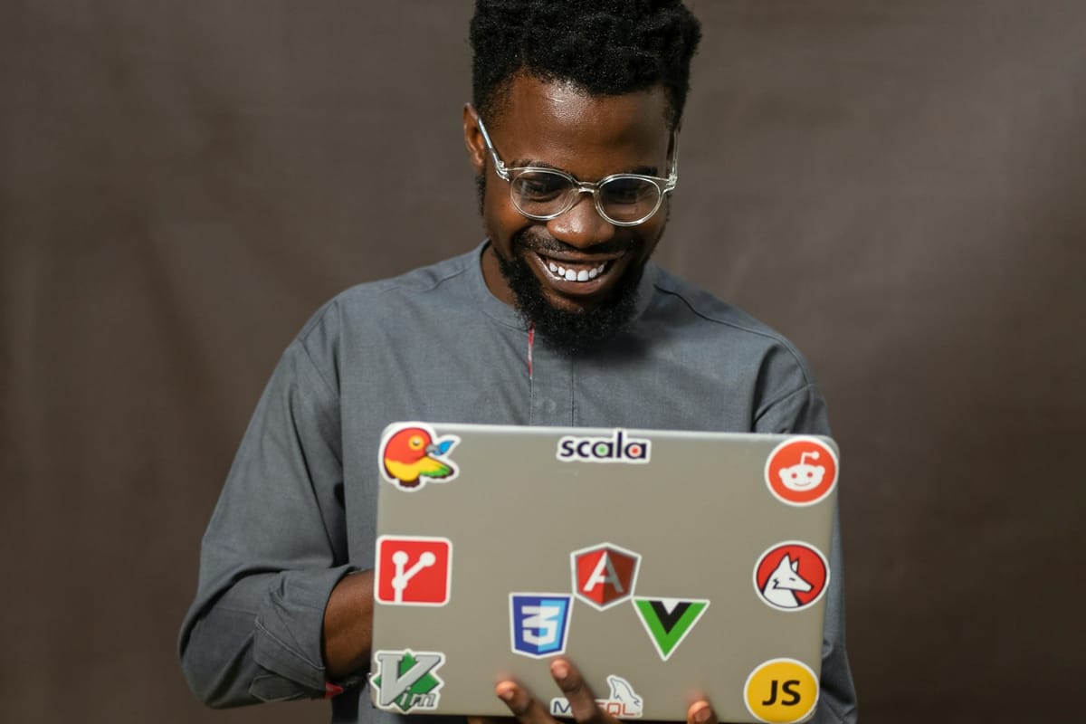 A smiling man holding a laptop covered in coding stickers