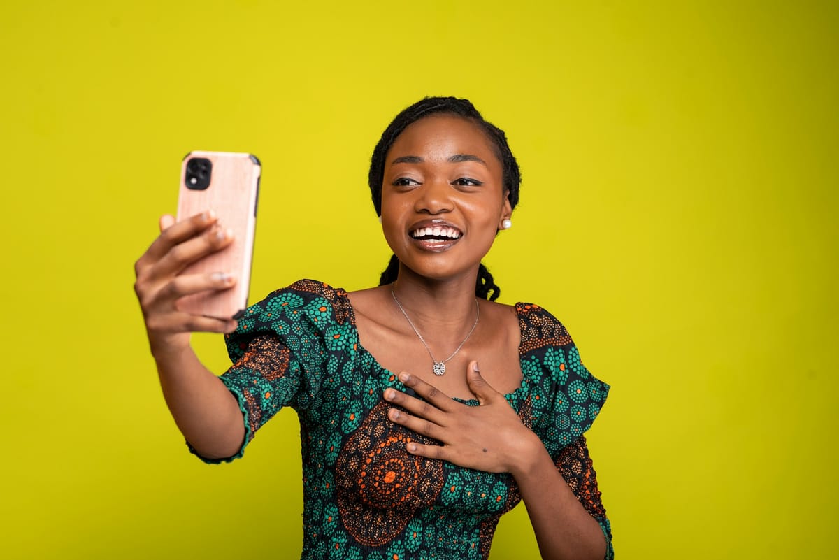 A happy woman in a patterned dress holding up her phone