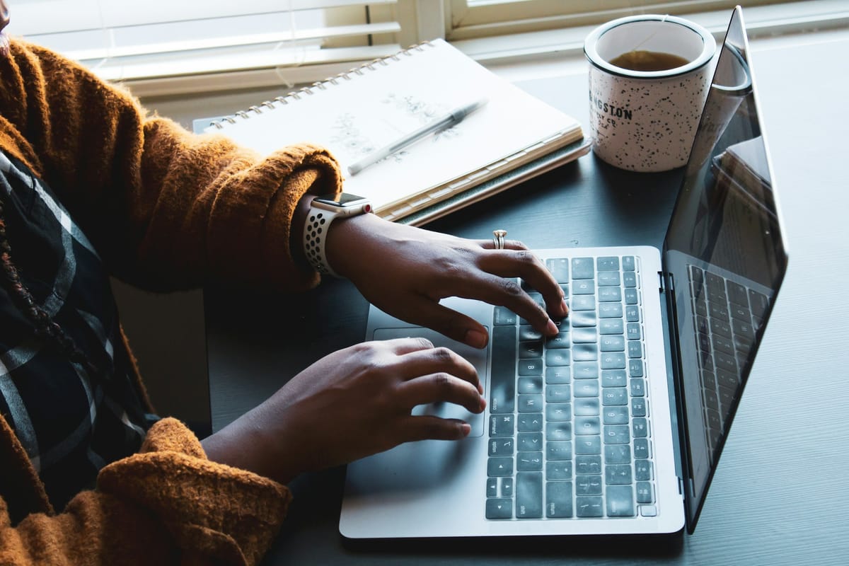 Hands typing on a laptop beside a cup of coffee