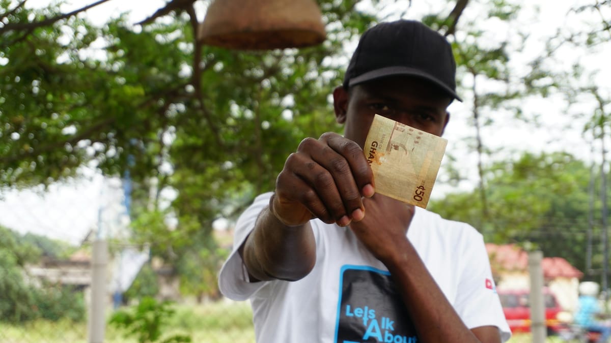A man holding up a Ghana cedi banknote outdoors