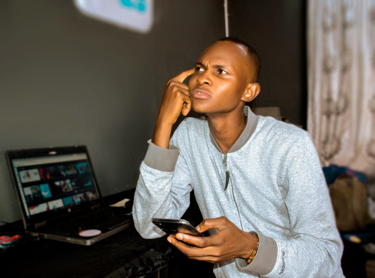 A frustrated man looking at his phone beside a laptop