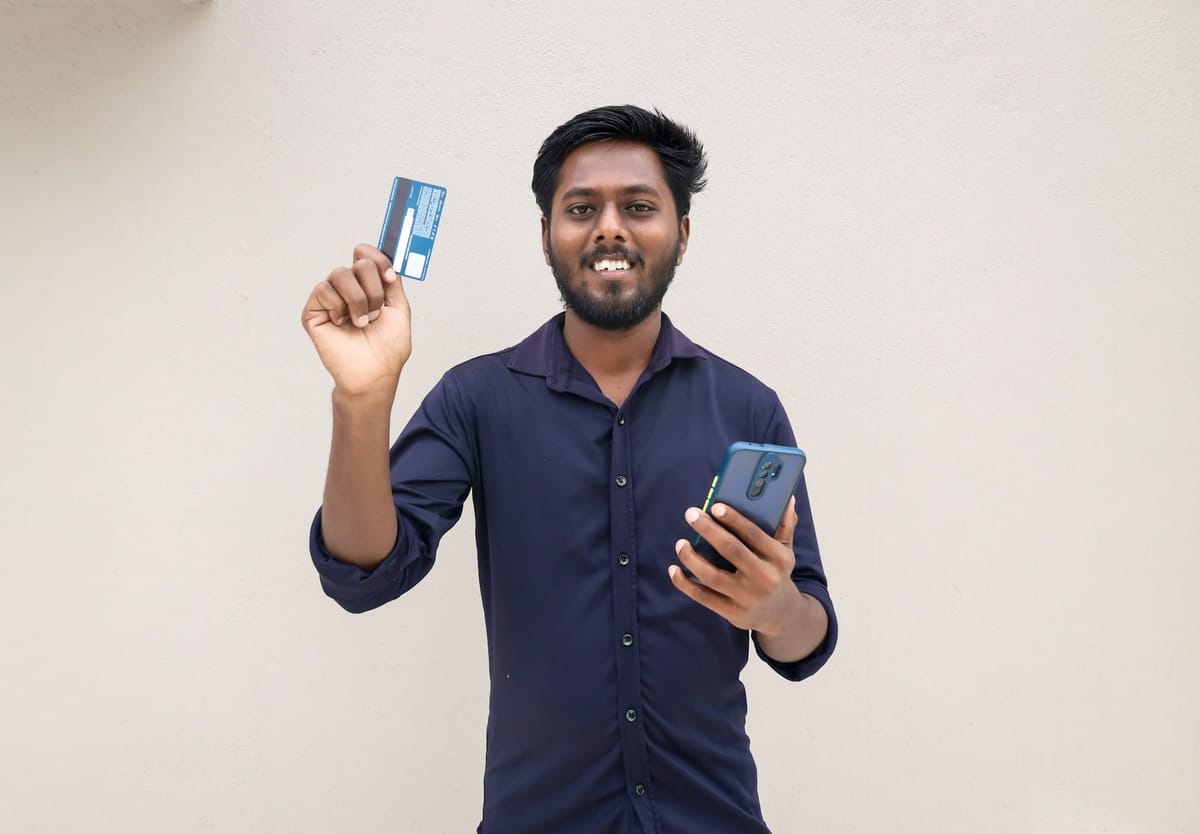 A smiling man holding a bank card and a smartphone