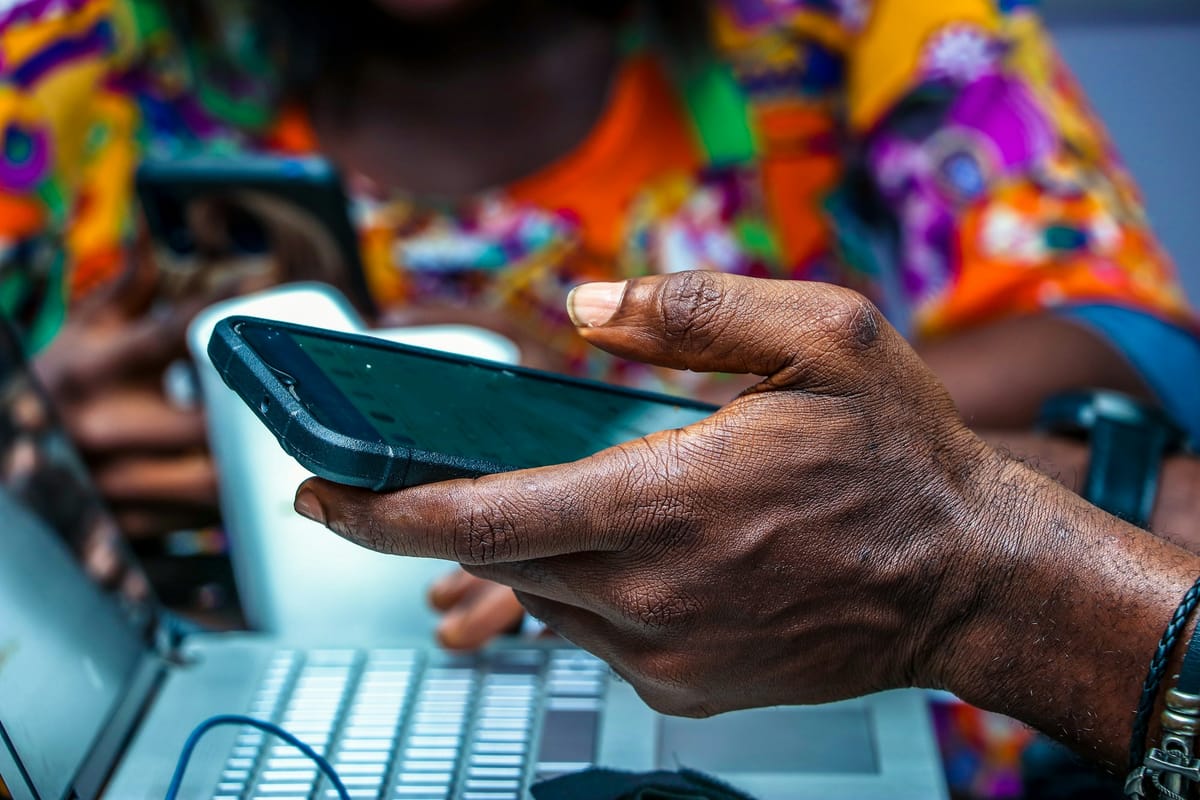 A hand holding a black Android smartphone above a laptop