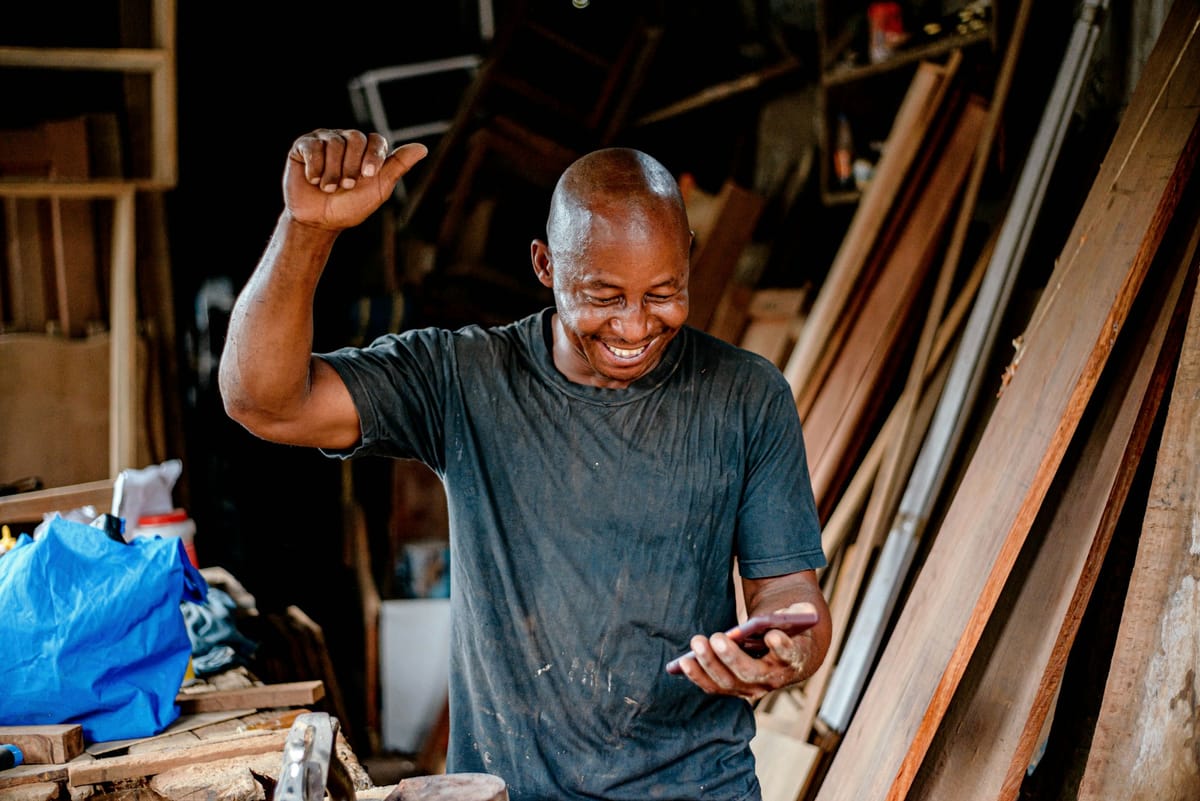 A smiling carpenter celebrating as he looks at his phone in a workshop