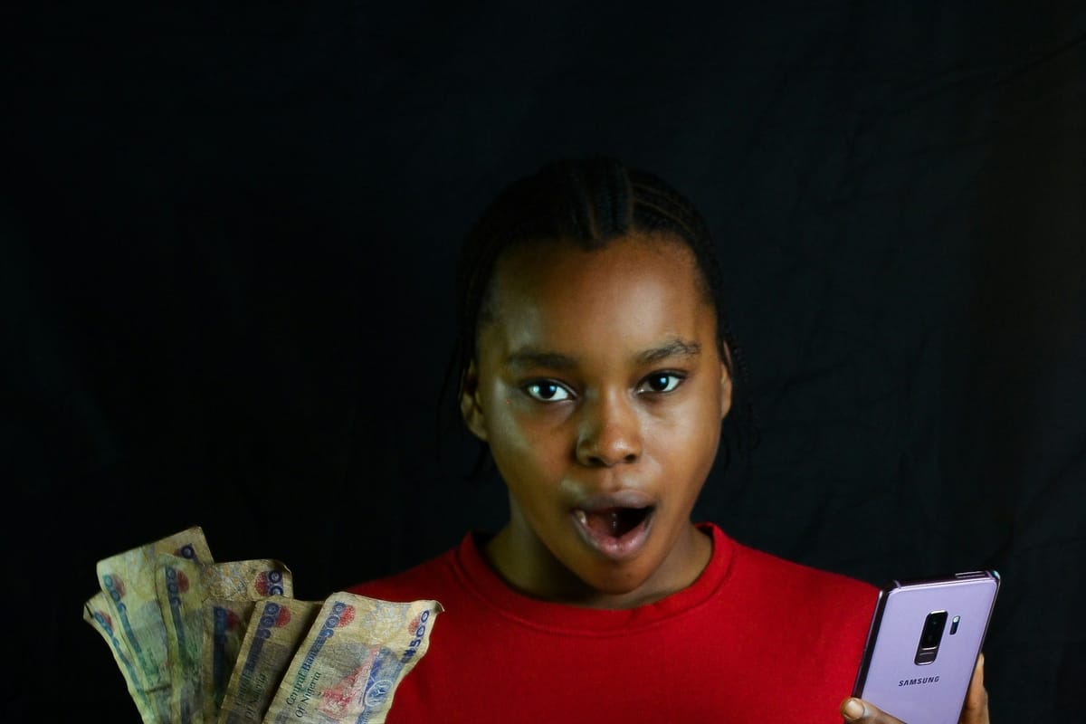 A surprised woman holding cash in one hand and a smartphone in the other
