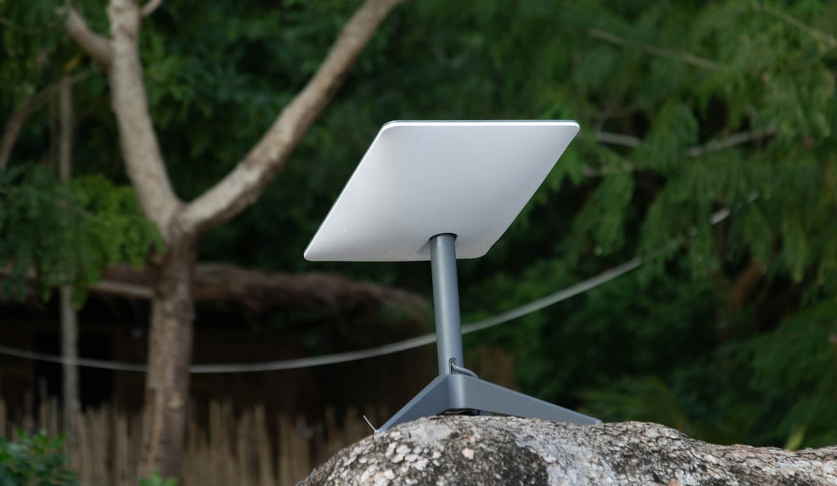 A white Starlink satellite dish on a stand among trees