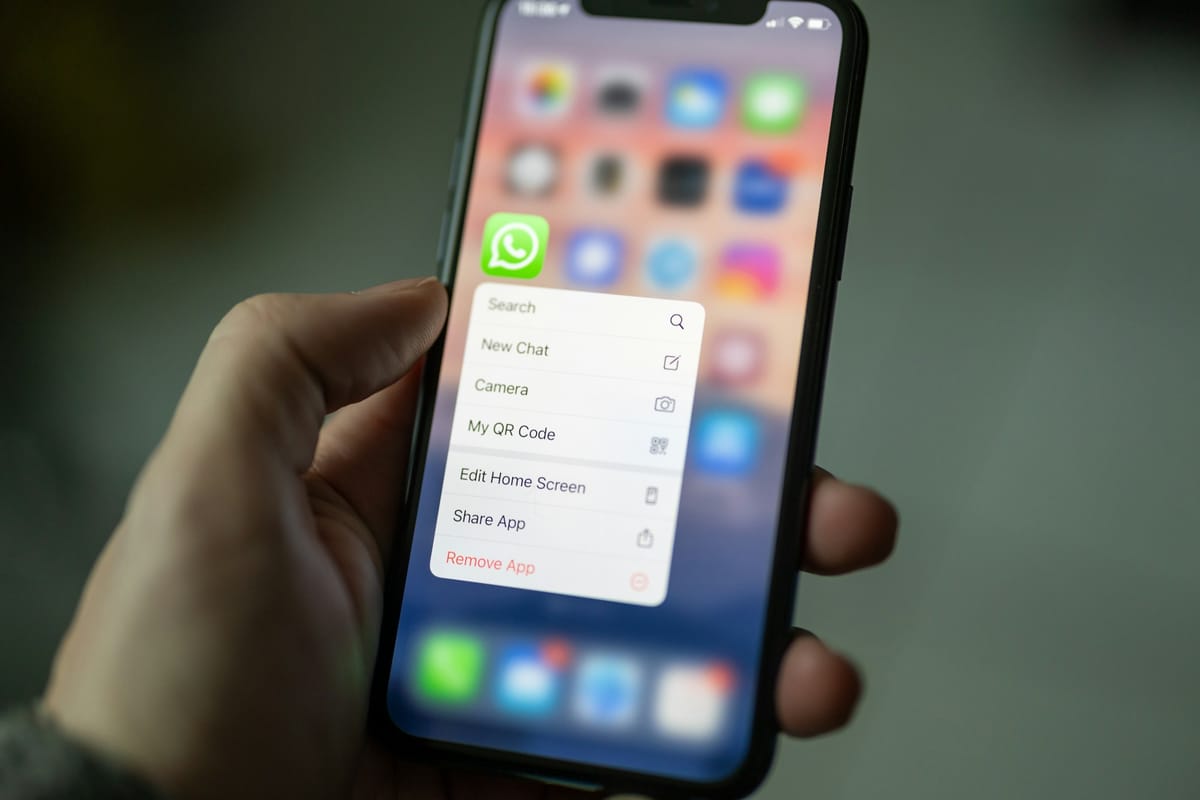 A hand holding an iPhone showing its app menu