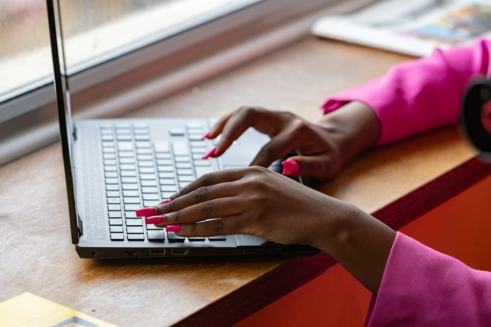 Hands typing on a laptop by a window