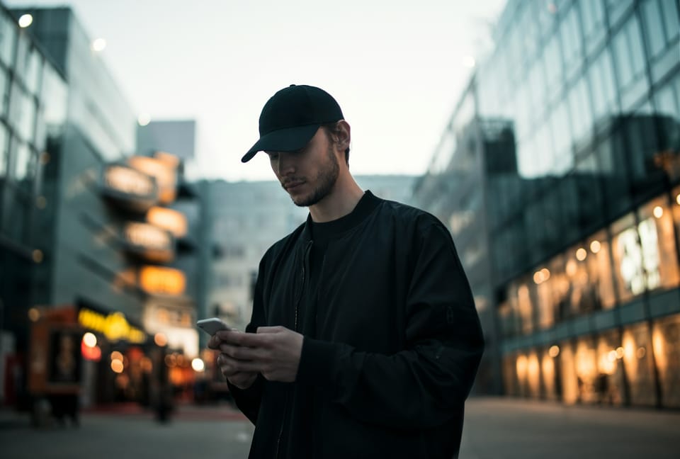 A man in a cap looking at his phone on a city street