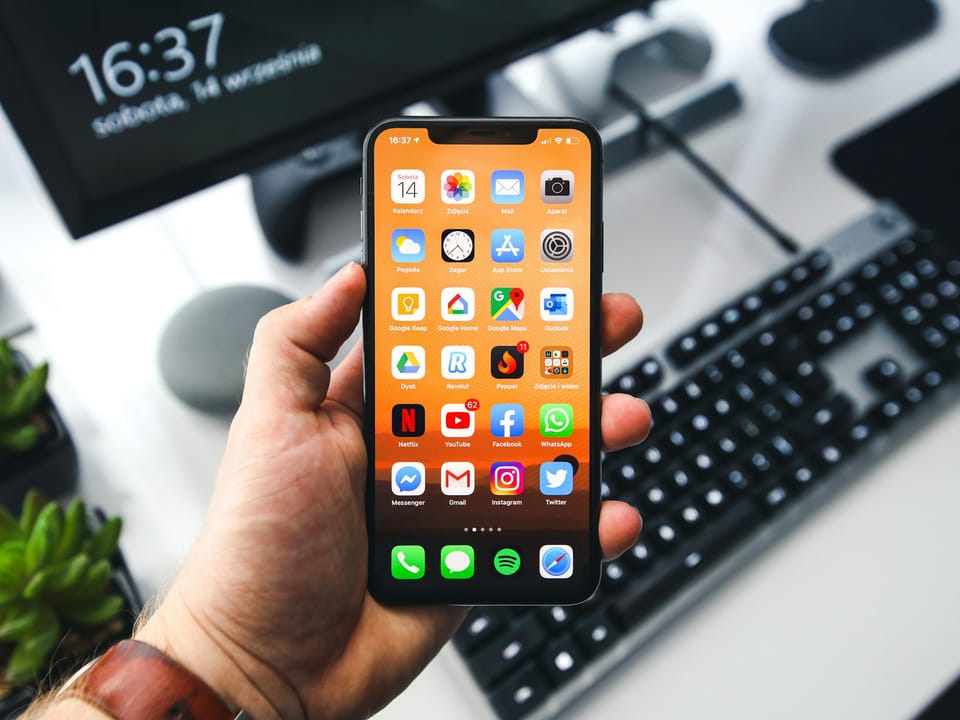 A hand holding a phone full of app icons by a keyboard