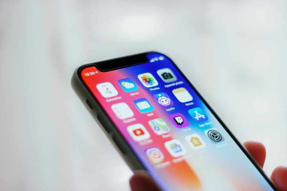 A hand holding an iPhone showing its home screen