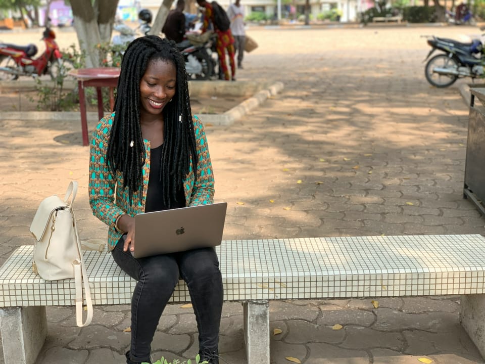 A smiling student with braids using a laptop on a bench