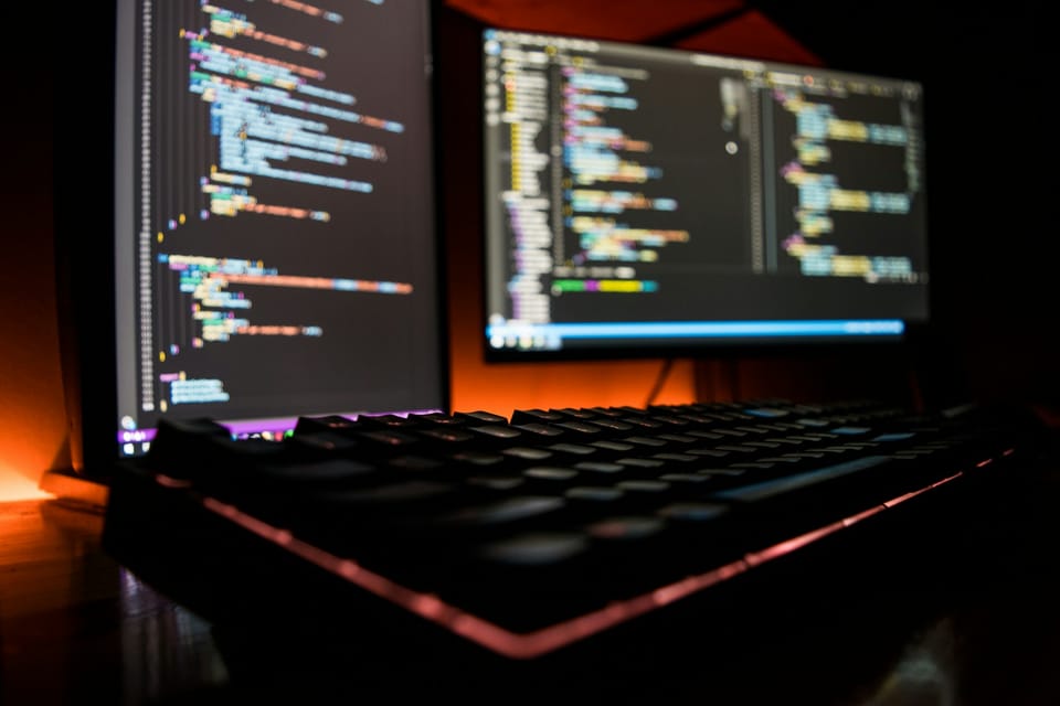 A backlit keyboard in front of screens full of code