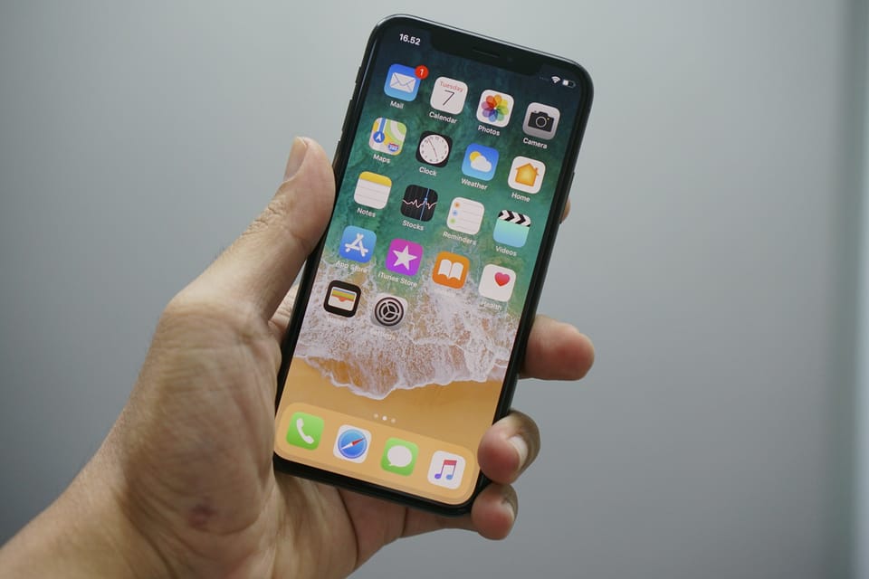 A hand holding an iPhone showing its home screen