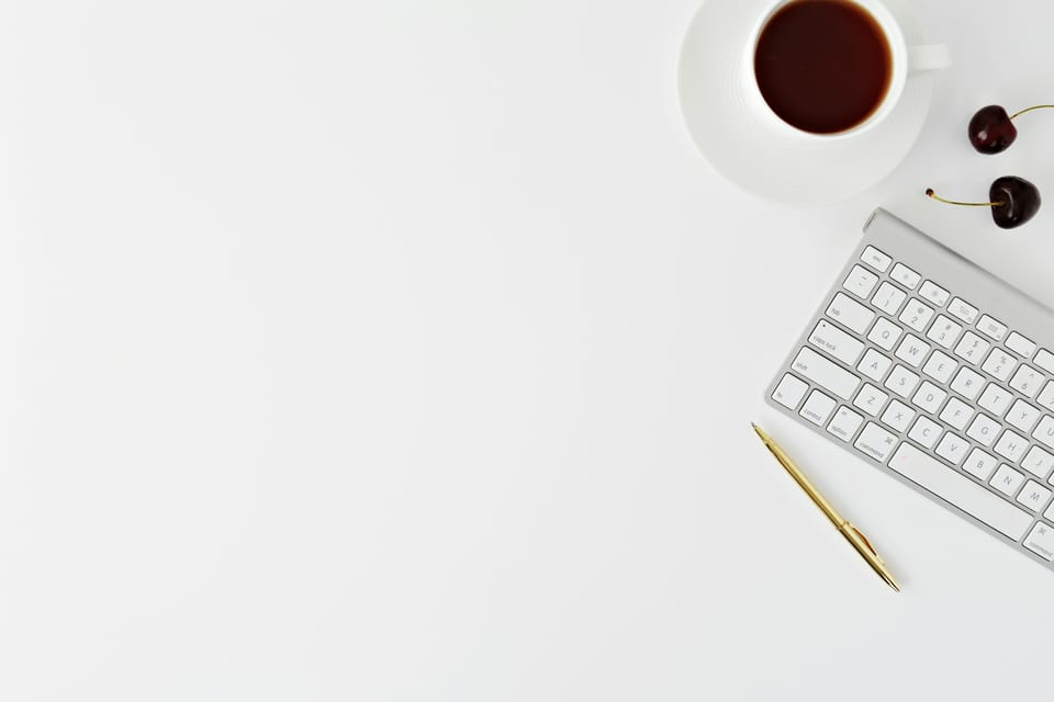 A keyboard, pen and cup of coffee on a white desk