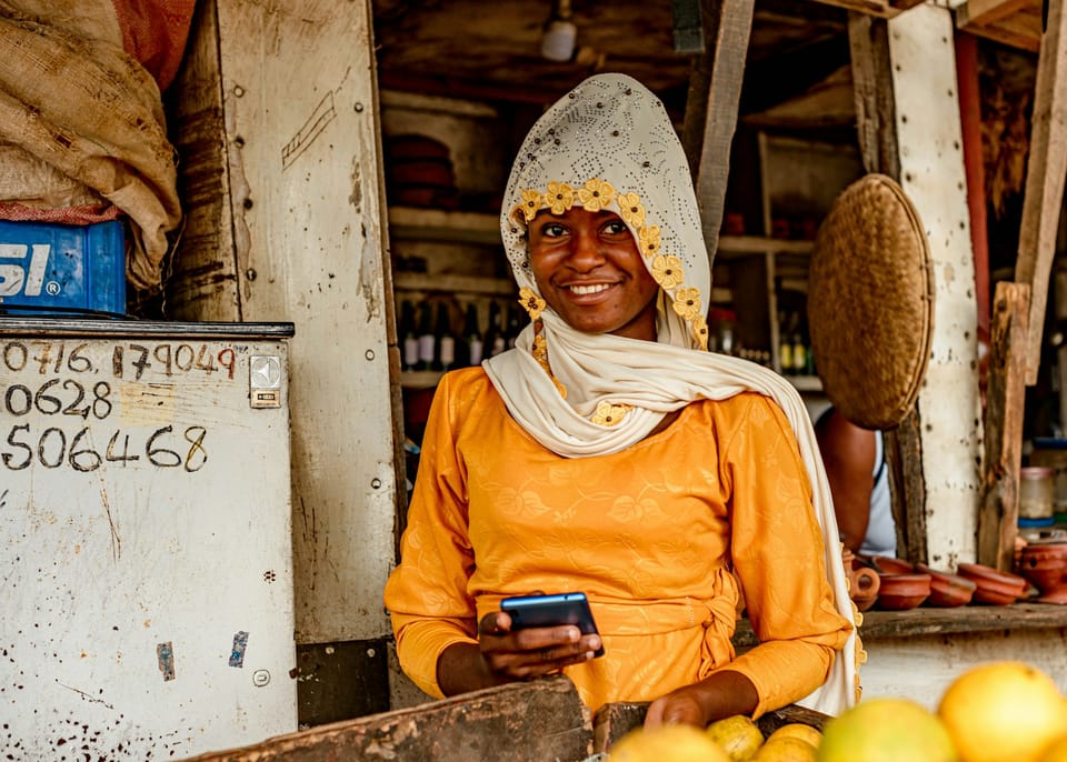 A woman at a fruit stand holding a mobile phone