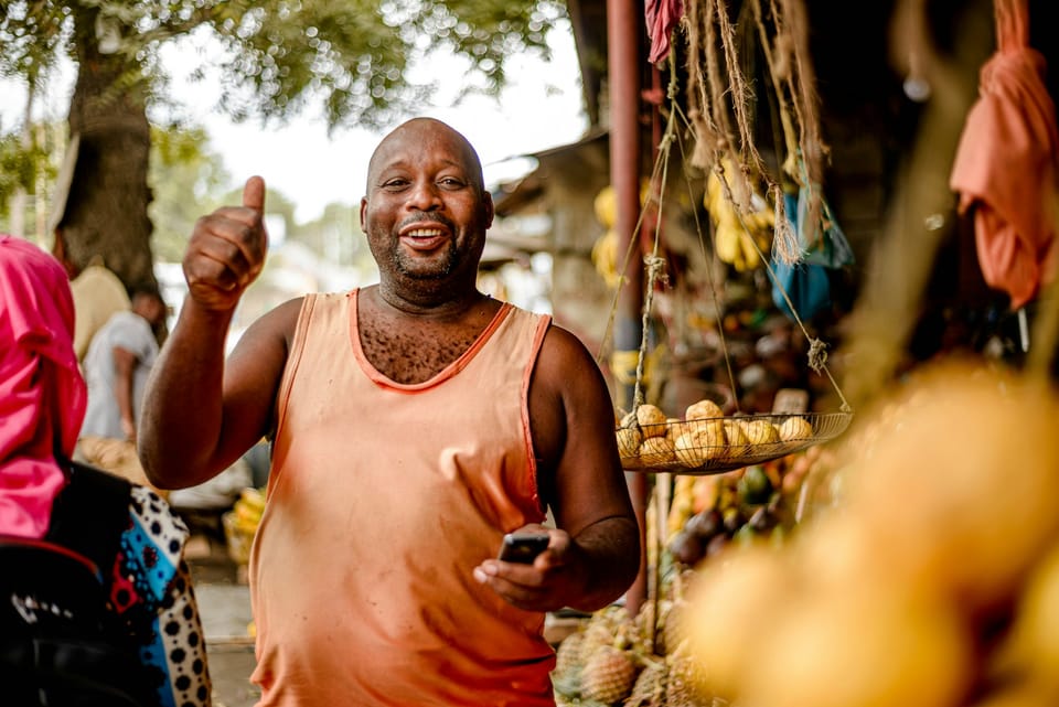 A man at a fruit stand giving a thumbs up