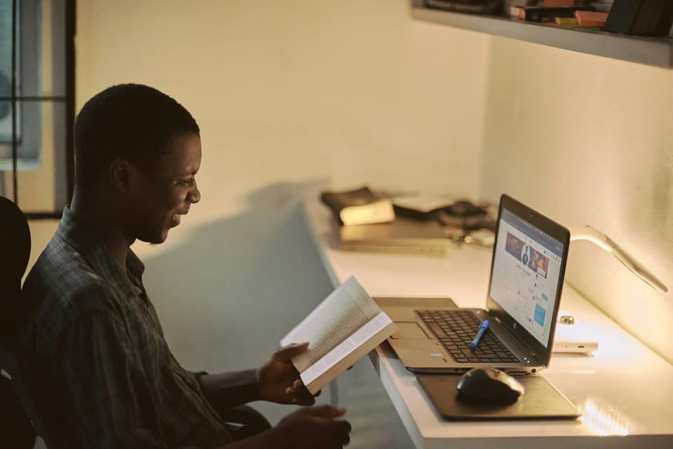 A man reading notes beside a laptop at a desk