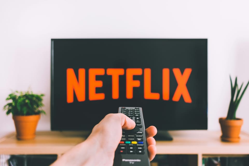 A hand holding a remote in front of a TV showing Netflix